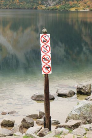 Tablice z zakazami czego nie wolno robić nad morskim okiem. słup wbity z tablicami nad brzegiem jeziora
