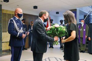 Anna Szpyruk otrzymuje z rąk ministra Mariusza Kamińskiego kwiaty i kopię karty z Księgi Pamięci na zdjęciu komendant Pani anna i policjanci asystujący w sali komendy głównej policji