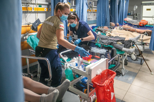 dwie pielęgniarki opiekują się pacjentem na łóżku szpitalnym