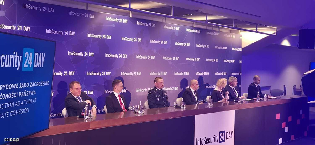 Komendant Główy Policji za stołem z innymi prowadzącymi konferencję.