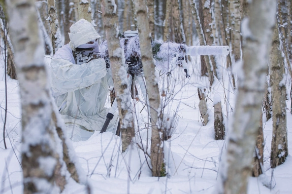 policjanci w białych kombinezonach ćwiczą na śniegu strzelanie wyborowe