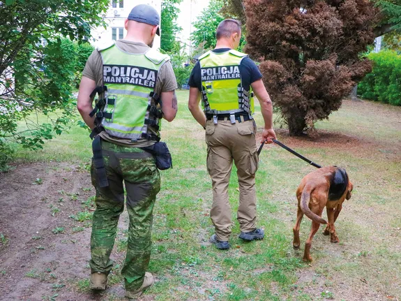 dwóch policjantów z psem oddalają się od fotografa