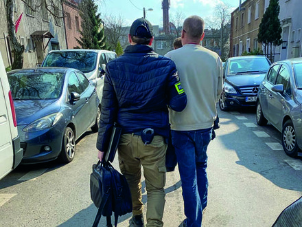 Policjant w cywilu  prowadzi zatrzymanego.