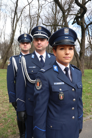 Policjantka w nowym mundurze, za nią dwaj policjanci również w nowych mundurach.