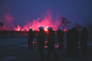 grupa policjantów stoi na tle płonących na czerwono flar