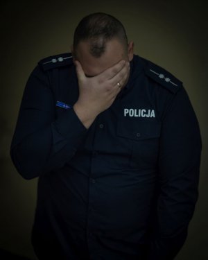 załamany policjant ukrywający twarz w dłoniach