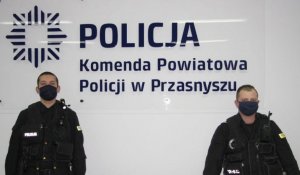 Paweł Lipka i Grzegorz Opalach przy ścianie z napisem Policja