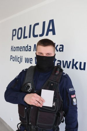 sierż. Adam Usurowski stoi na tle napisu policja z notatnikiem w ręce prawej trzyma go na wysokości swojego serca