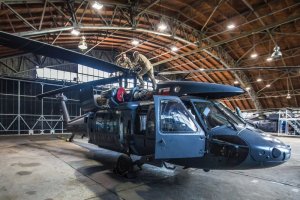 Prace hangarowe są ważnym elementem w utrzymaniu sprawności maszyn helikopter stoi w hangarze pootwierane kraty i mechanicy chodzący po śmigłowcu