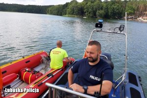 asp. Przemysław Matczak siedzi na łodzi pływającej na jeziorze obok ratownika w łodzi