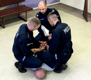 Przytrzymywanie osoby leżącej na brzuchu poprzez: dociskanie jej kolanami do podłoża  przez trzech policjantów (3)