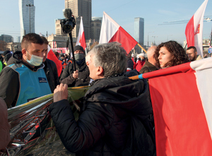 Bliskość obu grup stwarzała nerwowe reakcje. Między grupami ulokowali się policjanci z Zespołu Antykonfliktowego (ZAK). zdjęcie - policjant w kamizelce negocjuje z dwiema kobietami trzymającymi flagi polski