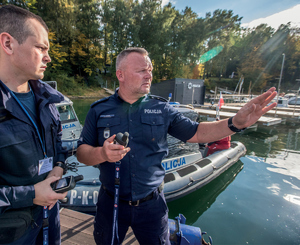 policjanci stoją na pomoście nad jeziorem. dowódca wskazuje na zadania do wykonania na wodzie