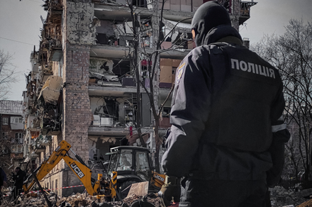 foto z ukrainy policjant ukraiński przy zbombardowanym budynku w tle koparka
