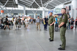 w hali na lotnisku, ochroniarze rozglądają się w tłumie ludzi