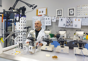 laboratorium z mikroskopami i zdjęciami owadów. Na środku mężczyzna w kitlu