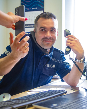 policjant przy biurku odbiera kilka telefonów naraz