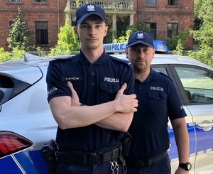 policjanci stoją przy radiowozach i przy budynkach pozując do zdjęcia do materiału