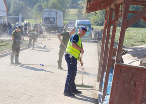 policjant sprząta szczotką podjazd zatopionego wcześniej urzędu