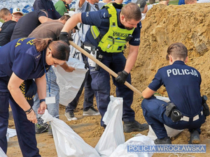 policjanci podczas powodzi ratują ludzi. sypią piach do worków, wynoszą na plecach z domów osoby, holują na pontonie poszkodowanych i ich dobytek