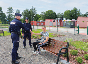 policjanci legitymują siedzącego na ław2ce młodzieńca