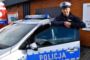 policjant stoi przy radiowozie i opiera się o drzwi radiowozu