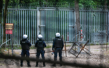 policjanci w pełnym umundurowaniu bojowym stoją przy płocie granicznym z białorusią