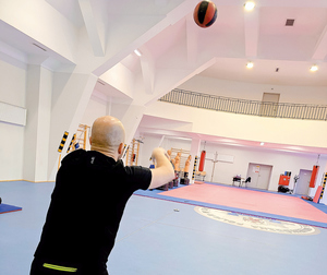 zawodnik ćwiczy na hali sportowej rzuty piłką, brzuszki, bieg
