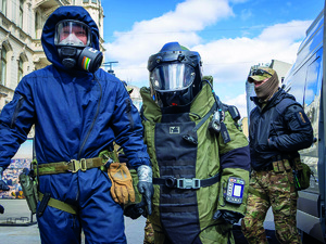 Dwaj policjanci w kombinezonach ochronnych oraz policyjny kontrterrorysta.