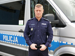 Policjant na tle służbowej furgonetki.
