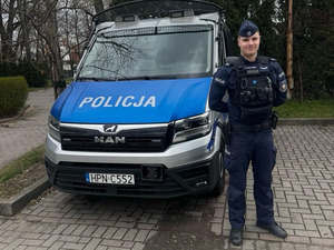 Policjant stoi przy służbowym furgonie marki man.
