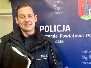 Policjant trzyma aktówkę, w tle rollup.