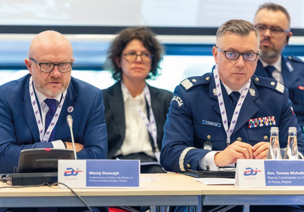 osoby siedzą za stołem. w tle kolejny rząd osób