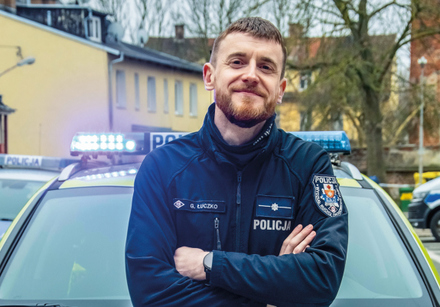 policjant stoi z przodu radiowozu
