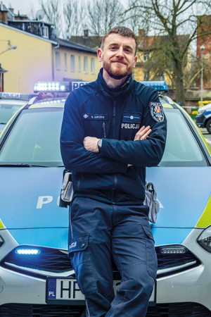 policjant stoi z przodu radiowozu