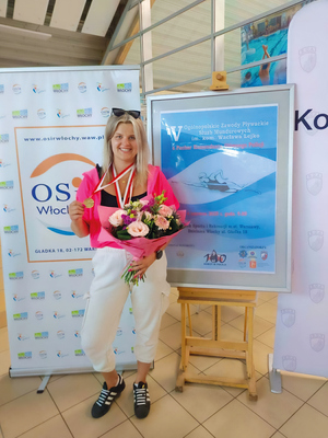 kobieta stoi przy plakacie zawodów. trzyma medal i kwiaty