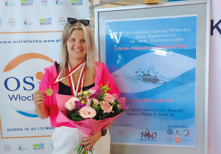 kobieta stoi przy plakacie zawodów. trzyma medal i kwiaty