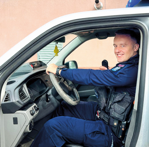 policjanci z materiału pozują do zdjęcia na tle budynków i radiowozu i w sali