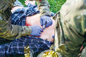 ratownicy ratują poszkodowanego, widać jak rozcinają ubranie na klatce piersiowej i udzielają pierwszej pomocy