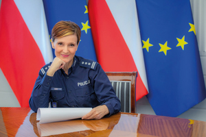 policjantka za biurkiem w tle flagi polski i UE