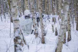 policjanci w białych kombinezonach ćwiczą na śniegu strzelanie wyborowe