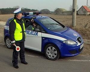 policjant z radarem i lizakiem stoi przy radiowozie