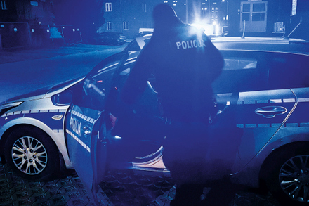 policjant stoi tyłem przy radiowozie nocną porą