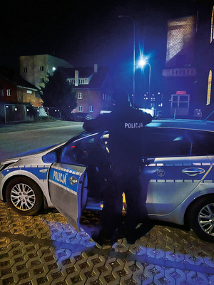 policjant stoi tyłem przy radiowozie nocną porą