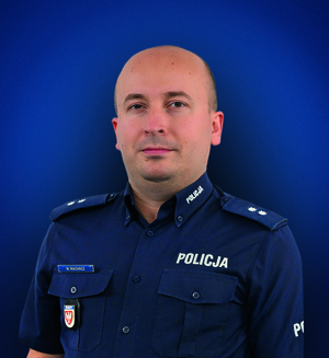 podkom. Marcin Wachacz pozuje na niebieskim tle.