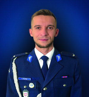 sierż. Adam Filipiak pozuje do zdjęcia na niebieskim tle.